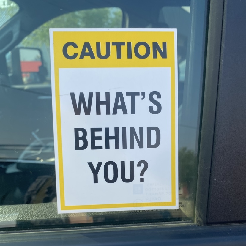 sticker on a truck window that reads 'caution: what's behind you?'