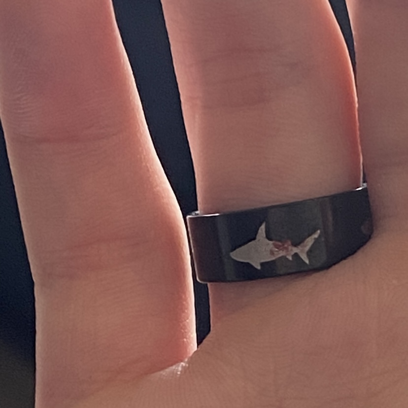 black ring with a silver shark silhouhette covered with a red smudge
